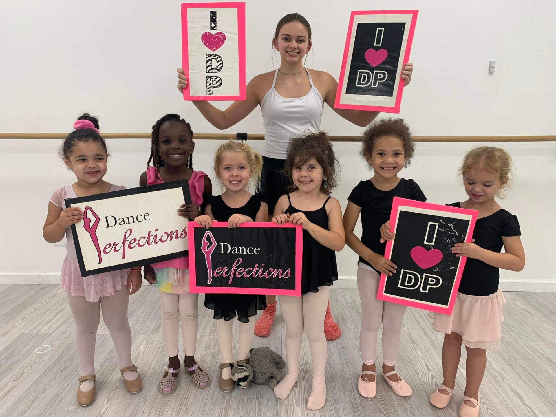 A preschool ballet class holding I Love DP signs with their teacher