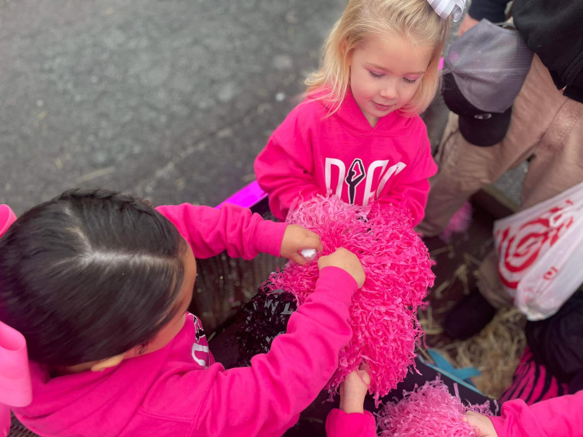 A teacher handing pink pom-poms to a little dancer before the parade
